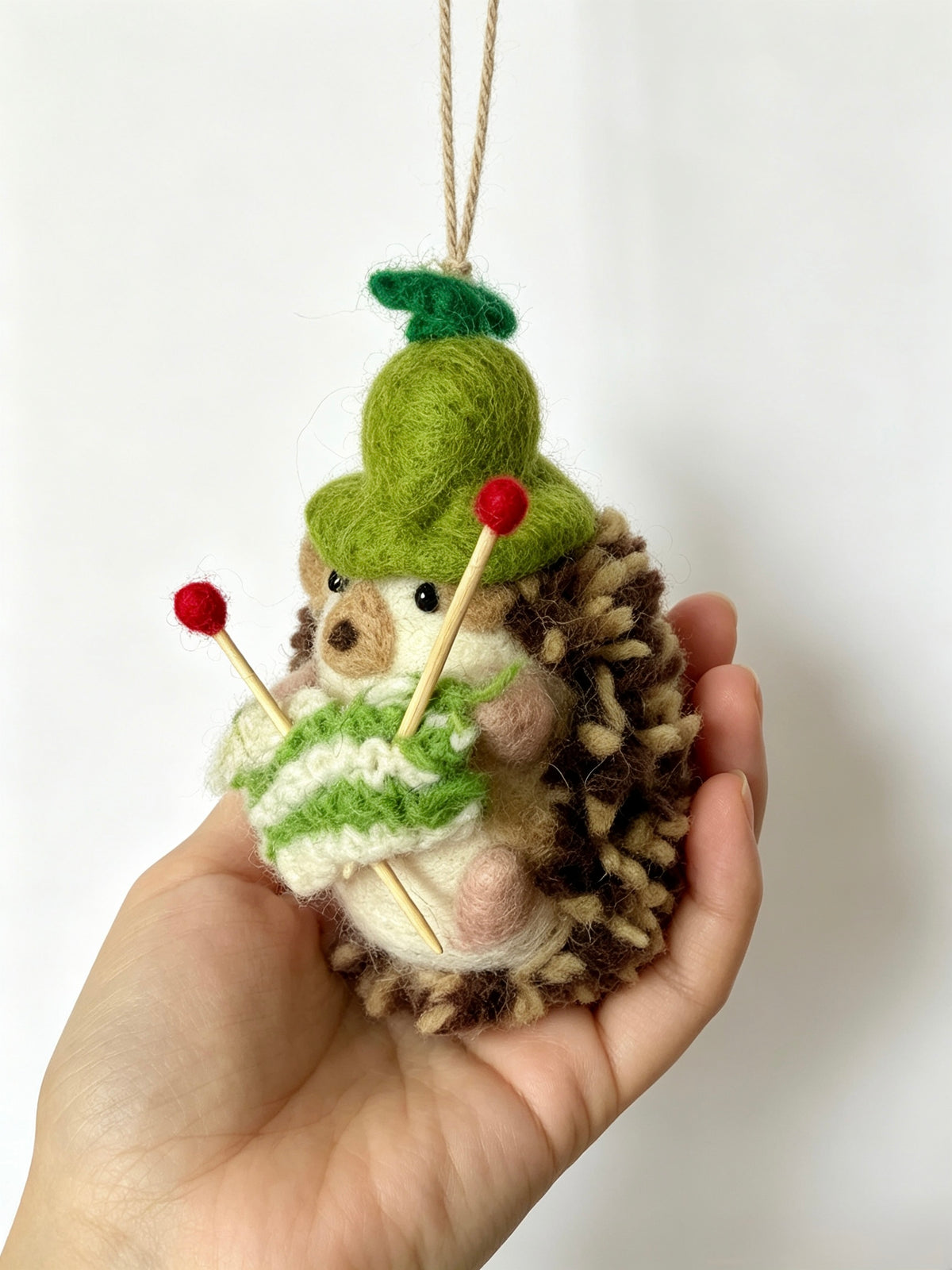 Side view of handmade wool felt hedgehog hanging decoration with knitting needles