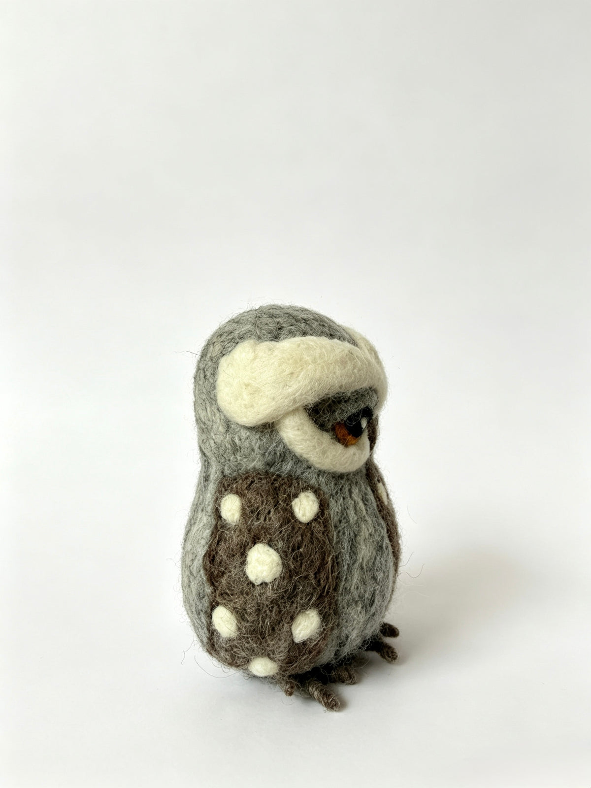 Side view of handmade wool felt owl figurine on a white background