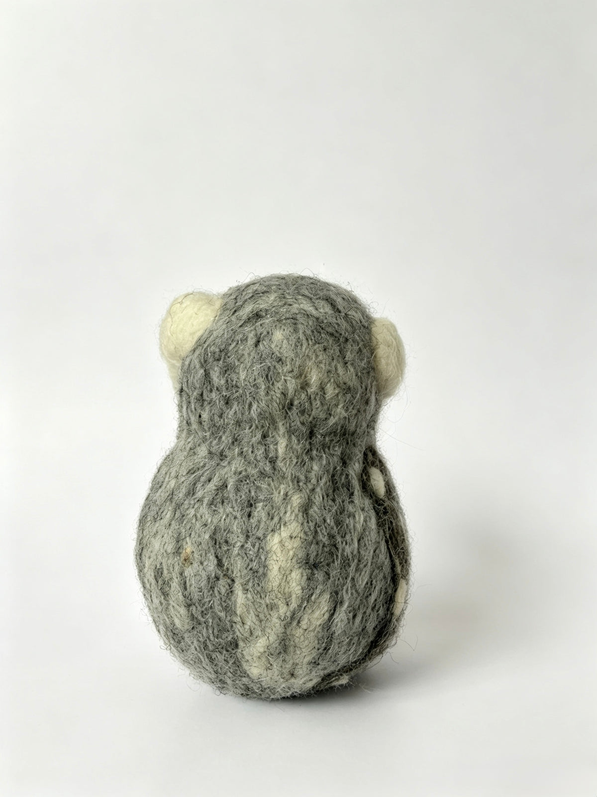 Rear view of handmade wool felt owl figurine against a soft pastel background