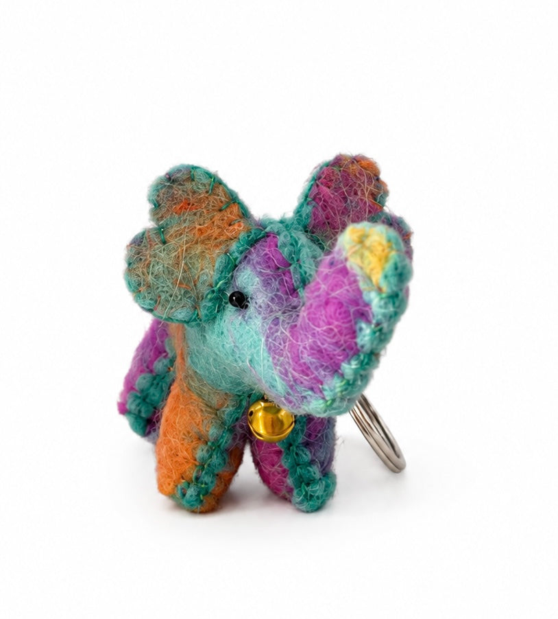 Colourful handmade elephant keyring with gold bell photographed in a flower meadow