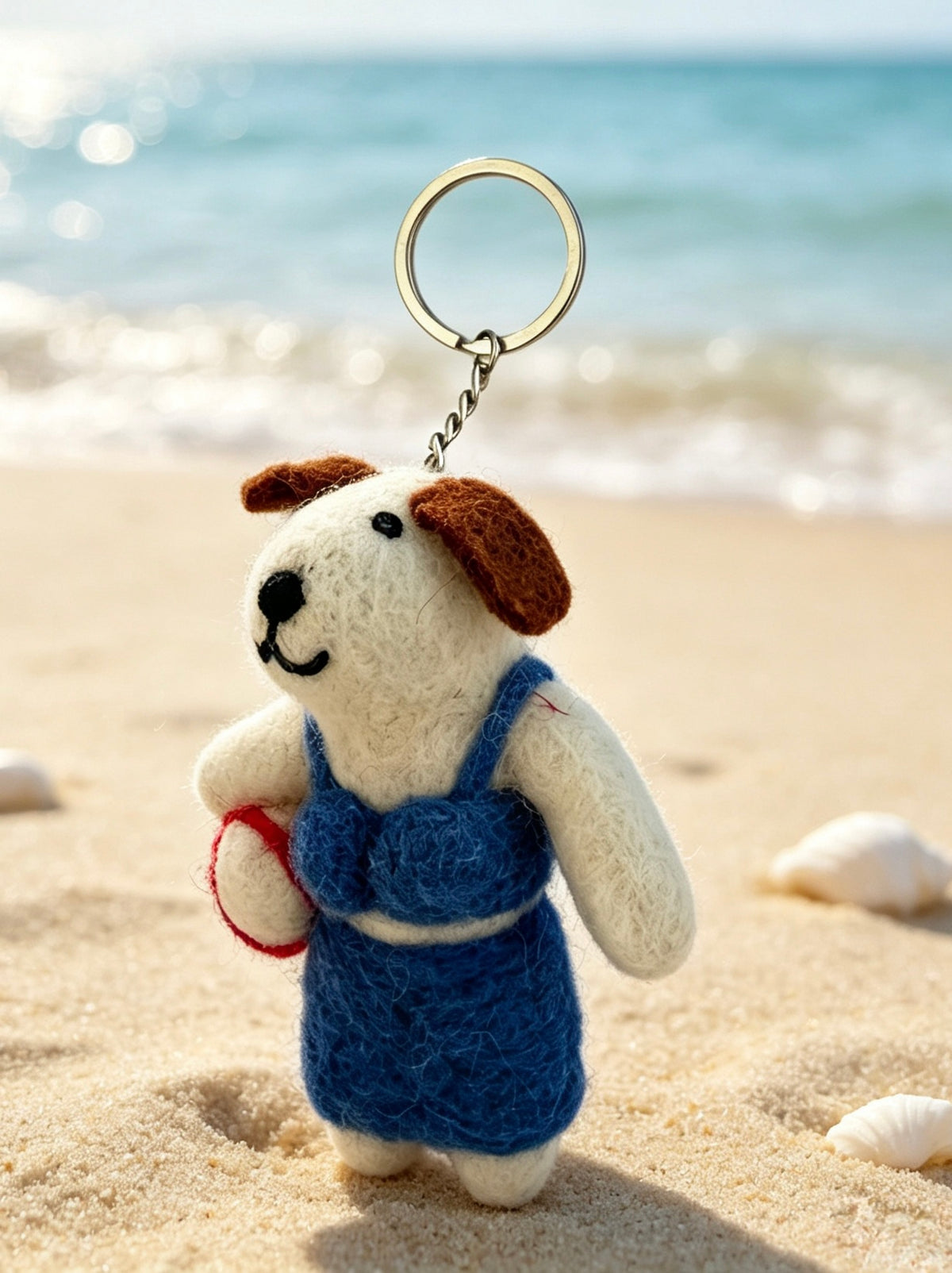 Handmade wool felt dog keychain photographed on a sunny beach